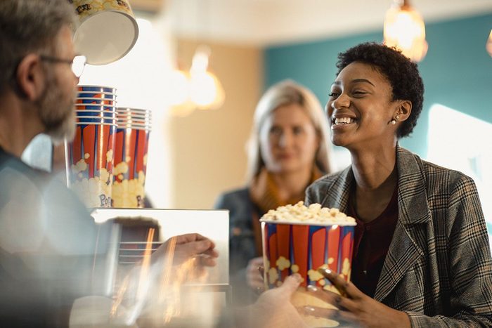 Young female woman buying popcorn at the concession stand while at the movies. She is being passed the popcorn by the customer assistant.