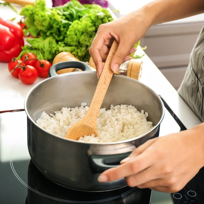 Woman cooking rice in saucepan on stove