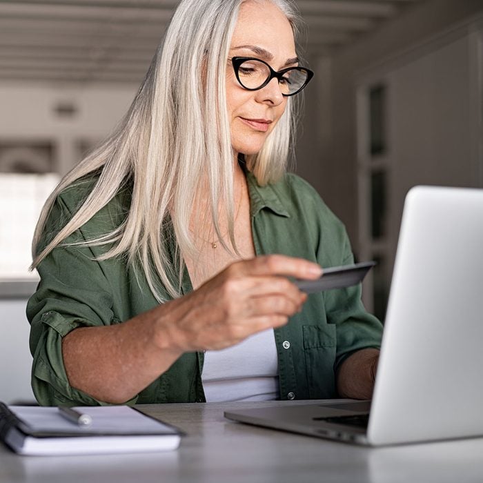 Mature woman using credit card making online payment at home. Successful old woman doing online shopping using laptop. Closeup of retired fashionable lady holding debit card for internet banking account.