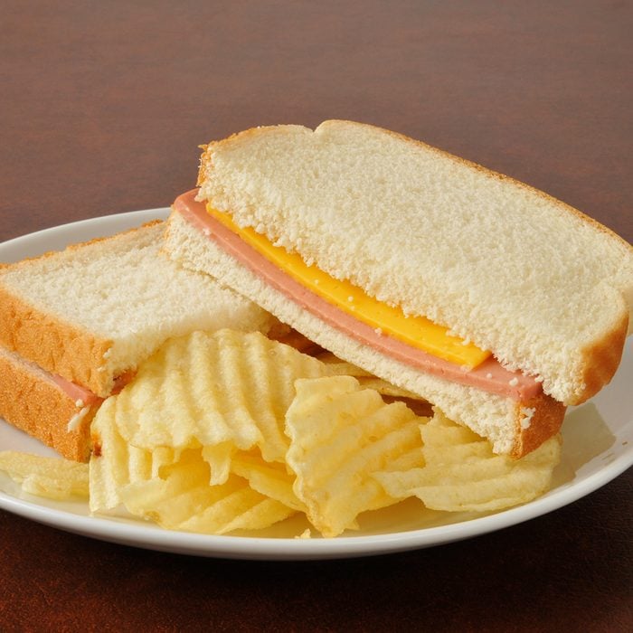 A bologna and cheese sandwich with potato chips