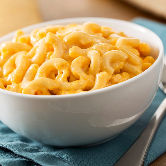 A white bowl of the best baked homemade macaroni and cheese on a table with a blue napkin. The recipe is made with elbow pasta and cheddar cheese. The shot is vertical and has selective focus. Macaroni and cheese is a American comfort food or soul food.