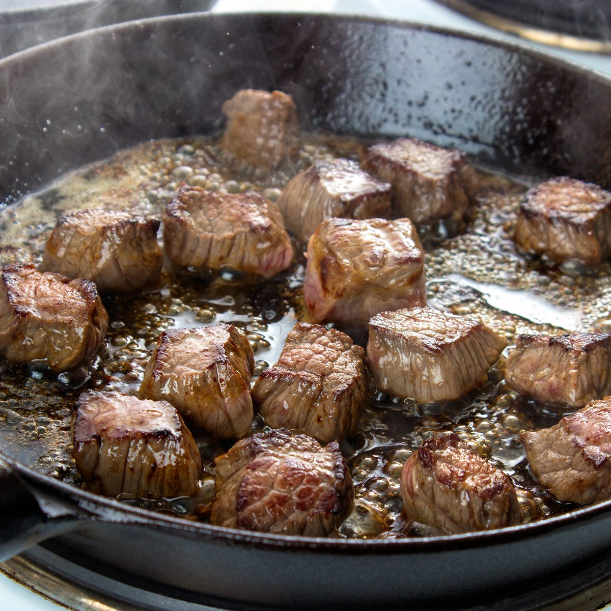 Frying beef bottom round roast cubes in cast iron skillet , meat flipped once