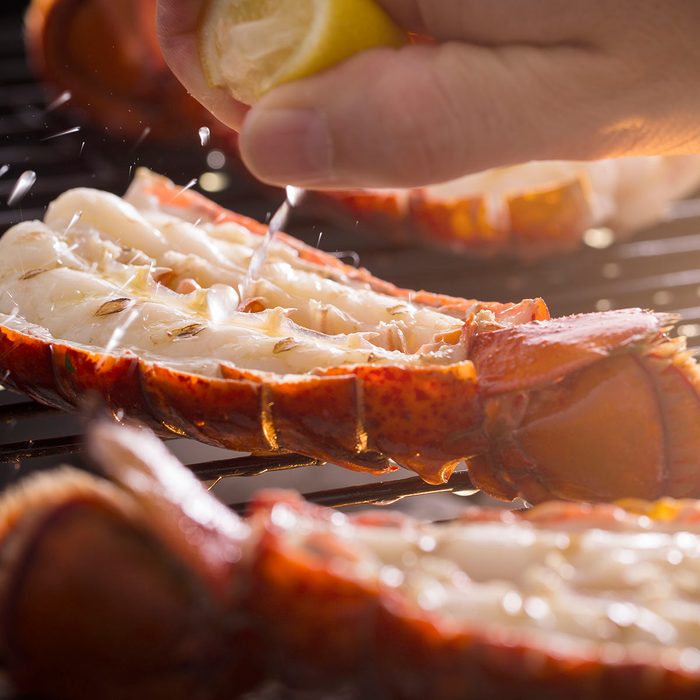 Fresh cold water lobster tails being cooked on a outdoor grill with fresh lemon juice being squeezed on the tails.