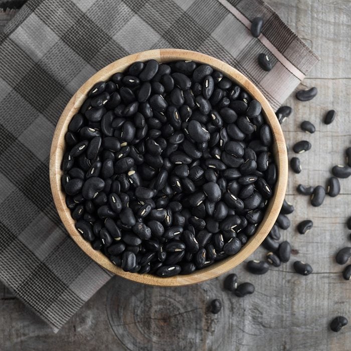 Black beans in a wooden bowl, black beans in a wooden spoon on a wood background