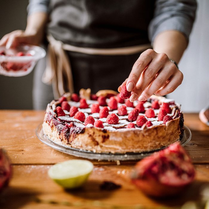 Woman Putting Raspberries To American Blackberry Pie, While It Is In Mold