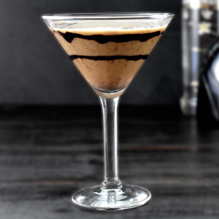 A chocolate martini with bottles of liquor in the background