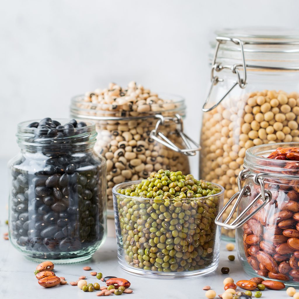 Healthy food, dieting, nutrition concept, vegan protein source. Assortment of colorful legumes in jars, lentils, soy kidney beans, chickpeas on a modern kitchen table. Copy space background