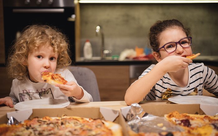 Portrait of cute little girls sitting and eating pizza