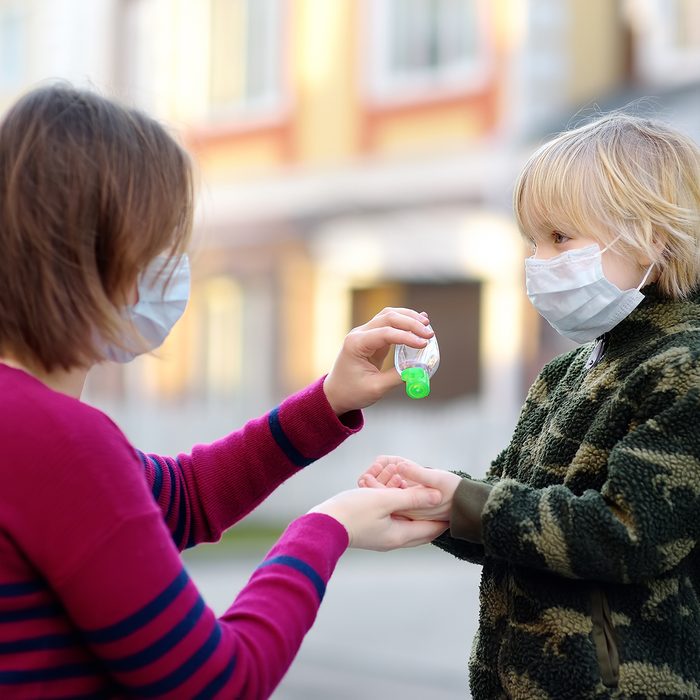 Young woman and little child wearing protective mask makes disinfection of hands with sanitizer in airport, supermarket or other public place. Safety during COVID-19 outbreak. Epidemic of virus covid