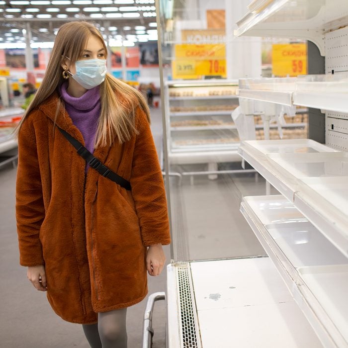 Young woman in medical mask and empty shelves in supermarket