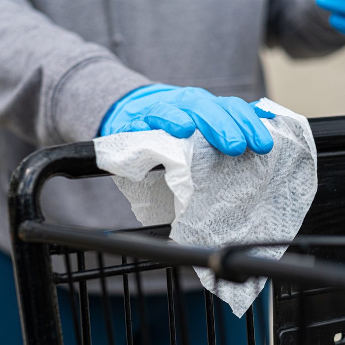 Shopper wearing gloves to prevent the coronavirus covid-19 uses a disinfecting wipe to clean the handle of a shopping cart.