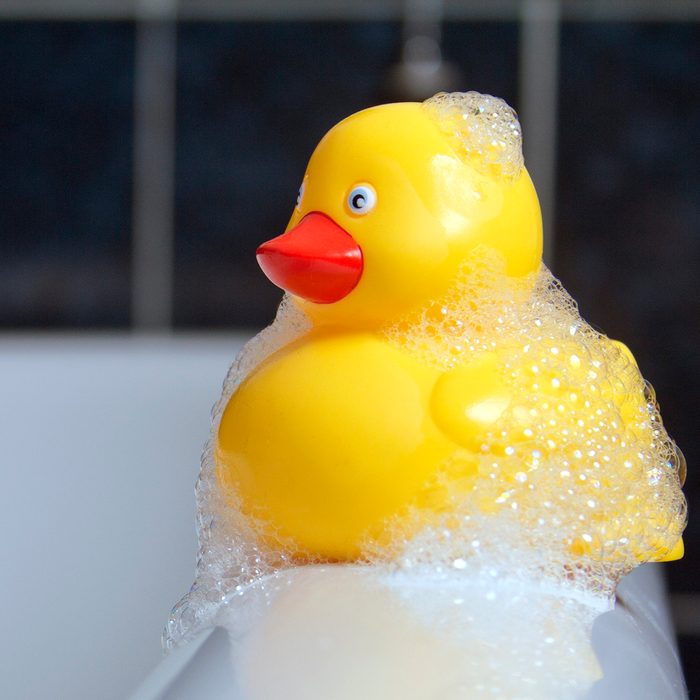 Yellow rubber duck with bubbles on sitting on the rim of a roll top bath