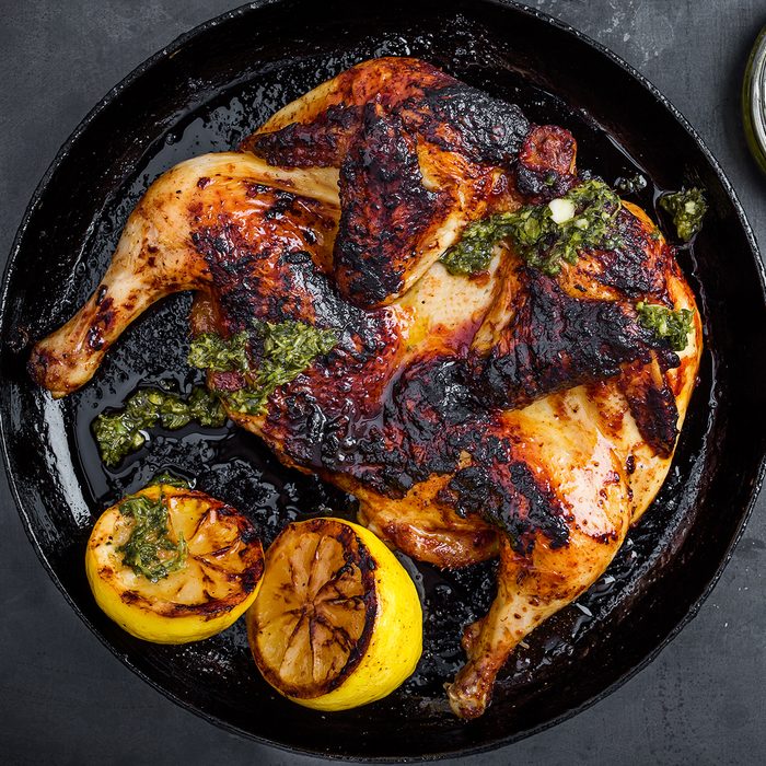 Barbequed chicken with chimichurri sauce in rustic cast iron pan on gray ready to eat, top view