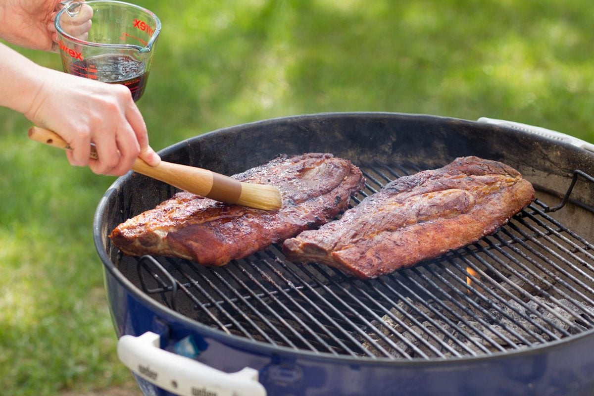 adding barbecue sauce to ribs on grill