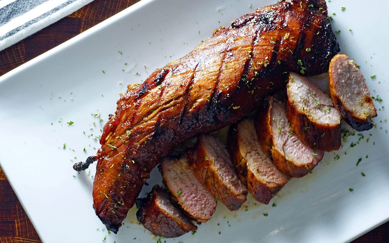 finished grilled pork tenderloin on a white platter and sliced