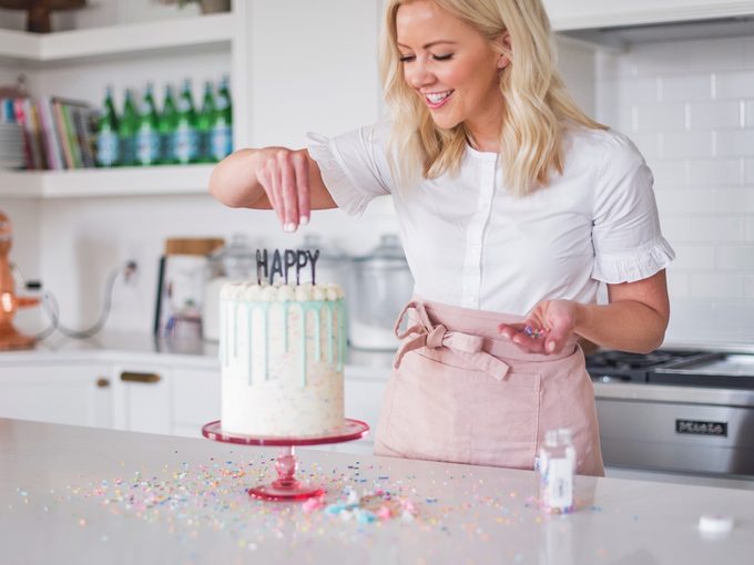 Blogger Courtney Rich decorates birthday cake on kitchen counter.