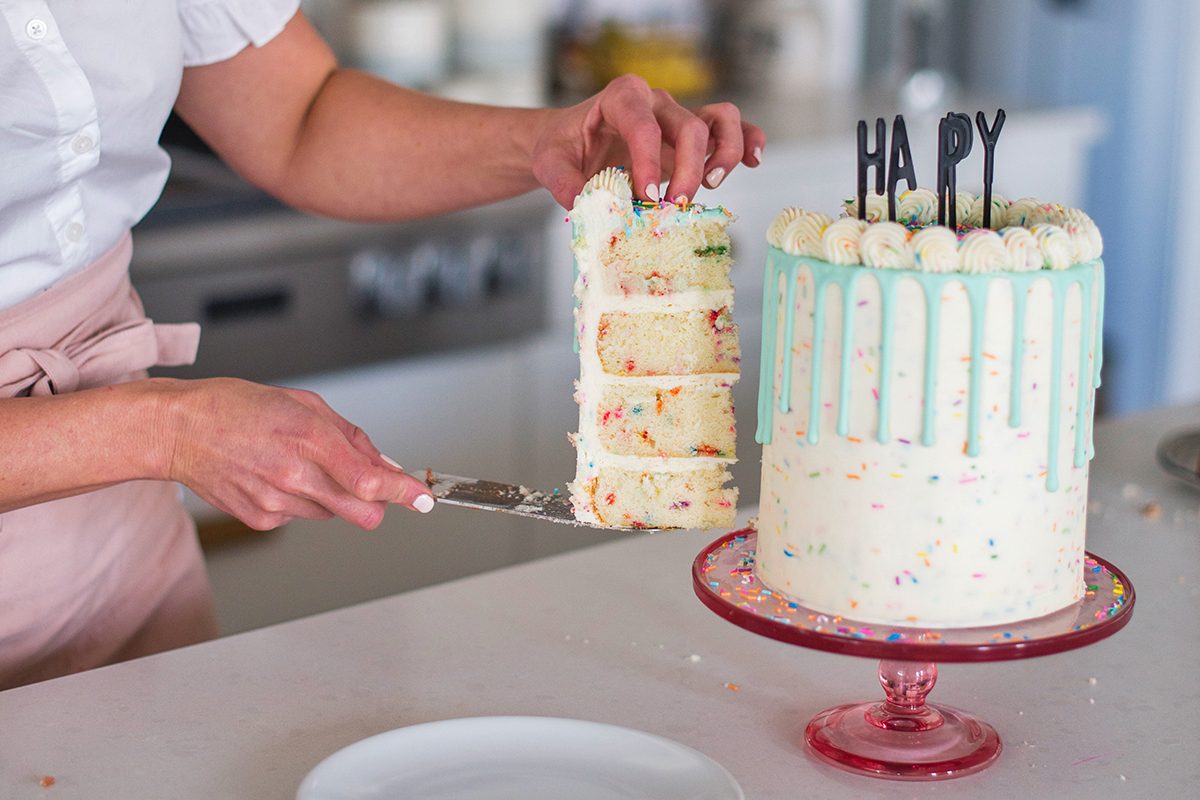 Tall layered birthday cake with drip icing being cut.