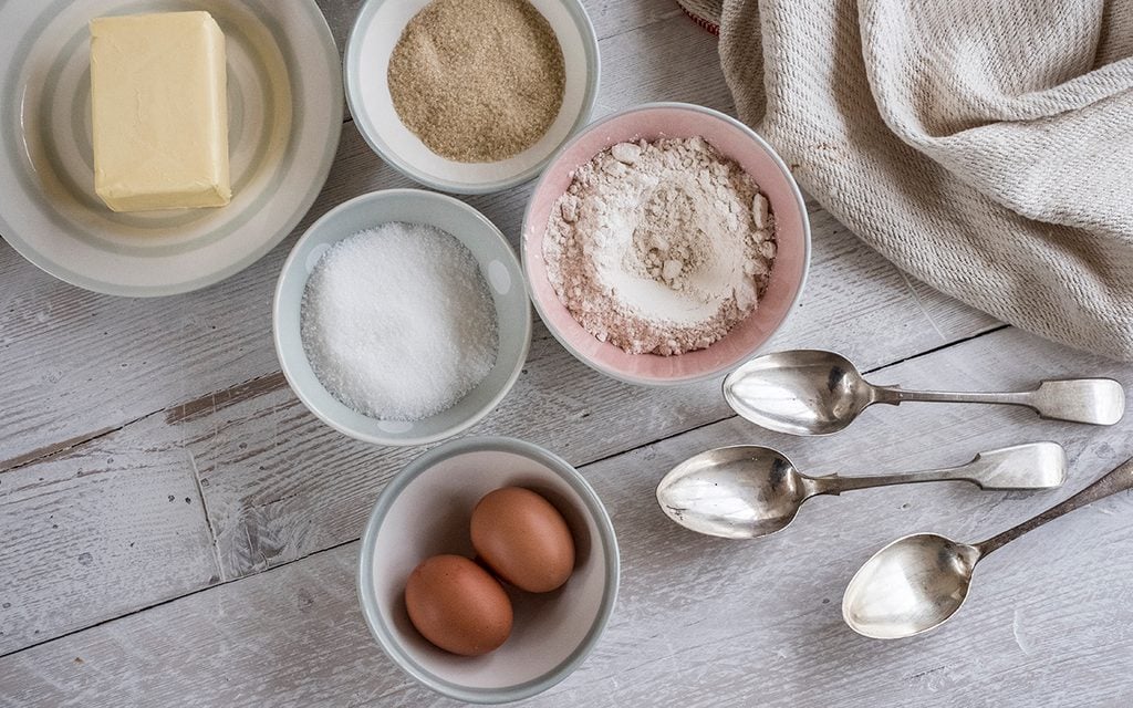 A table with ingredients for a baking project laid out, butter, sugar and flour, and two eggs.