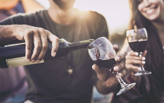 Close up of a couple drinking wine outdoors while man is pouring it into a glass.