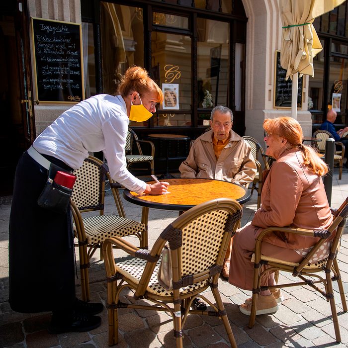 Waitress Stephanie Thiem (L) takes an order from guests Jens Krugmann (C) and Karin Fanselow (R) at the reopened Cafe Prag in Schwerin, northeastern Germany on May 9, 2020 amid the ongoing Covid-19, coronavirus pandemic. - The traditional cafe and restaurant welcomed sit in customers after two months of closure as restaurants in the state of Mecklenburg Western Pomerania were allowed to reopen under strict hygiene conditions Saturday, May 9, that saw a trickle of returning customers as the north eastern state and Germany are easing corona virus restrictions. (Photo by Odd ANDERSEN / AFP) (Photo by ODD ANDERSEN/AFP via Getty Images)