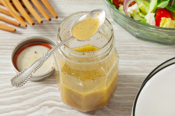 Greek Salad Dressing in a jar with a spoon on top