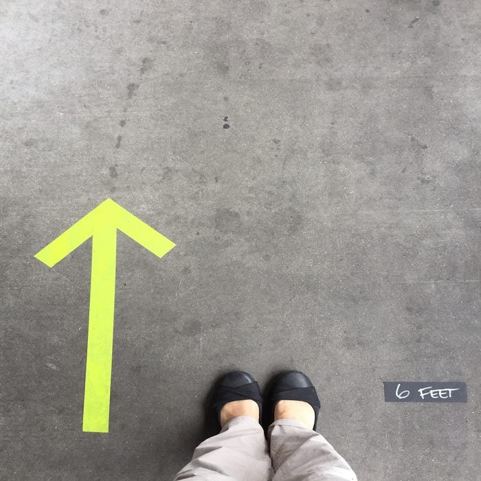 6 feet distance and the one-way direction is marked outside of a store where customers are waiting in a line to enter the store.