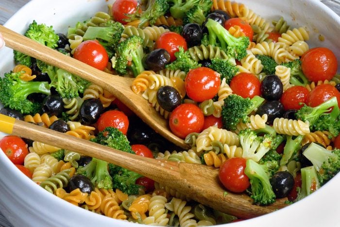 close up of Tri colored spiral pasta salad in a bowl with wooden spoons