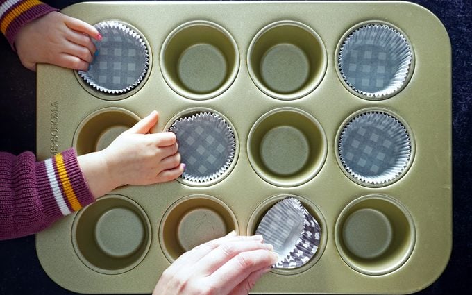 putting cupcake liners in a muffin pan with toddler