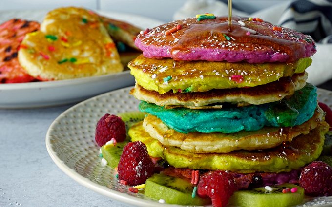 maple syrup poured over a stack of rainbow pancakes for kids