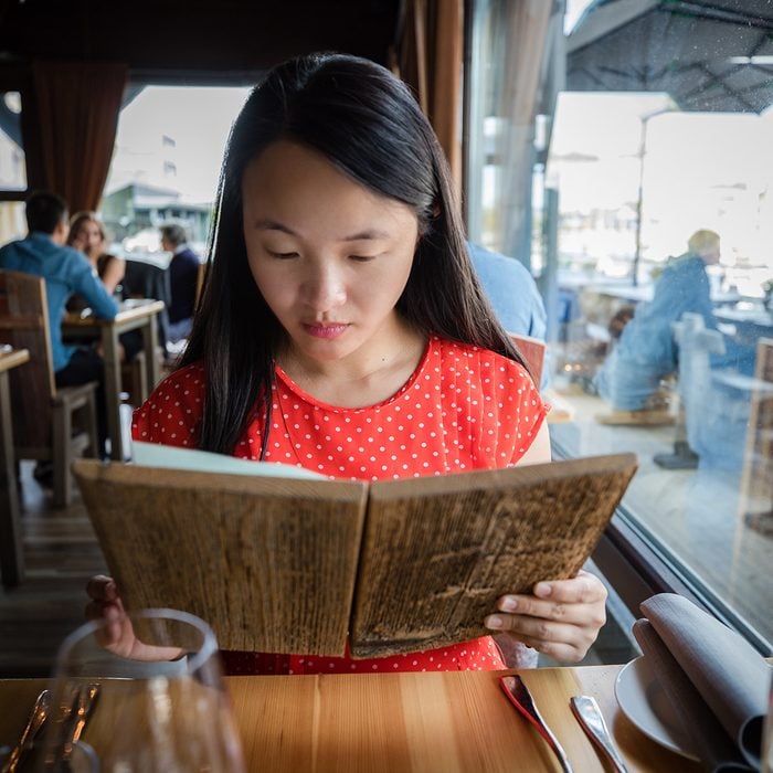 A young Chinese woman is carefully reading the menu made of wood at a restaurant on a fine day in Trondheim, Norway.
