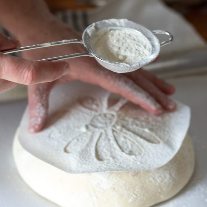 Sifting flour over a stencil on bread dough.