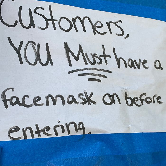 Close-up of a sign adhered on a small business commercial storefront window letting customers know in English that a protective face mask is required for entry.