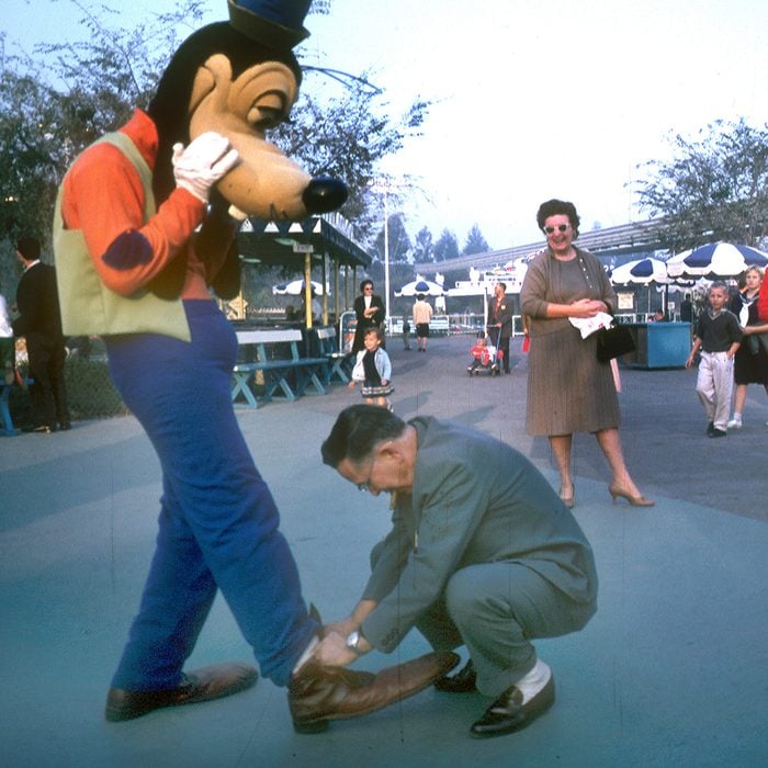 Disney character actor (played by photographer Tom Nebbia), dressed as Goofy, holds out his leg as a tourist ties his shoelaces at Disneyland, Anaheim, California, January 1962. (Photo by Tom Nebbia/Corbis via Getty Images)