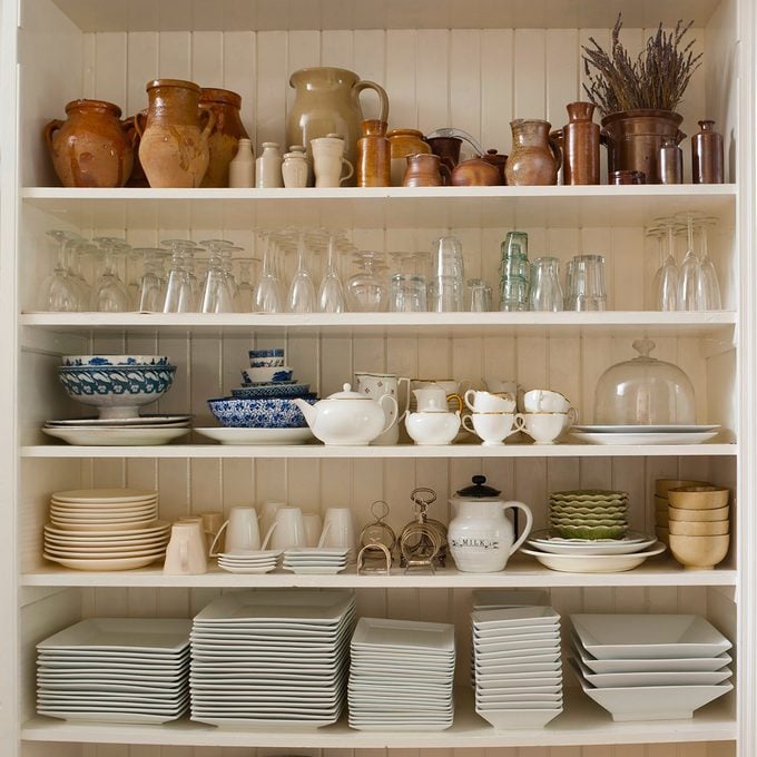 A variety of glassware, earthenware and crockery stored in an open white wooden shelf