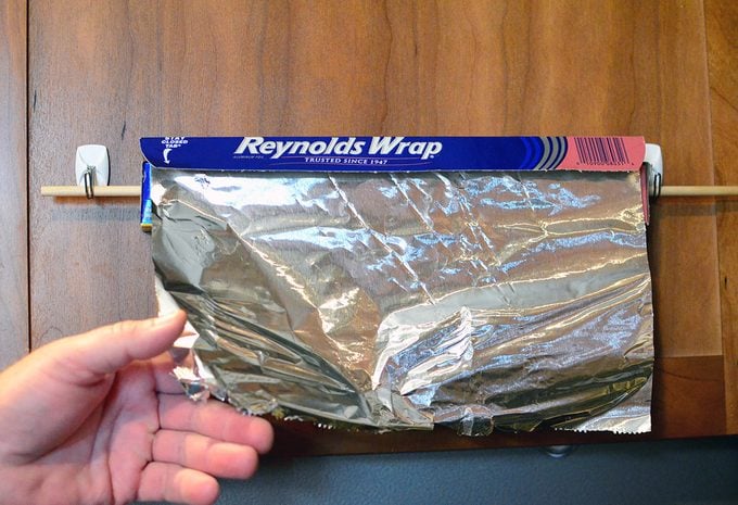 Man pulling foil off of DIY kitchen wrap storage organizer mounted on the back of a door.