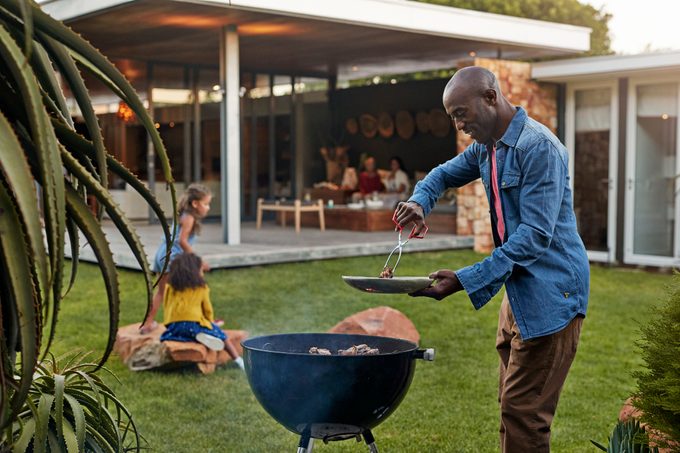 man grilling in his backyard with family