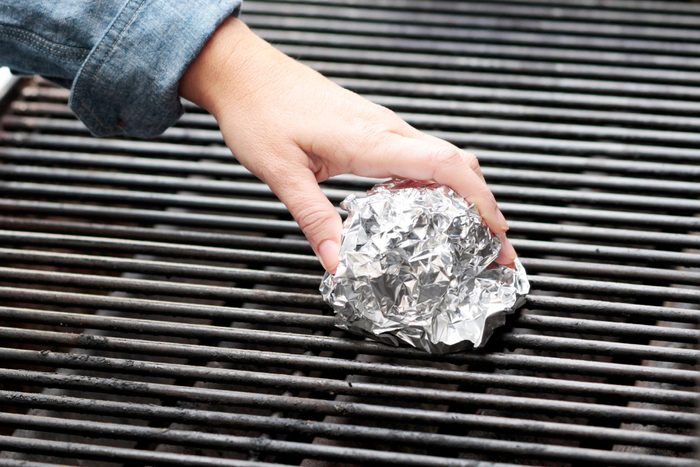 hand holding a ball of aluminum foil cleaning a grill