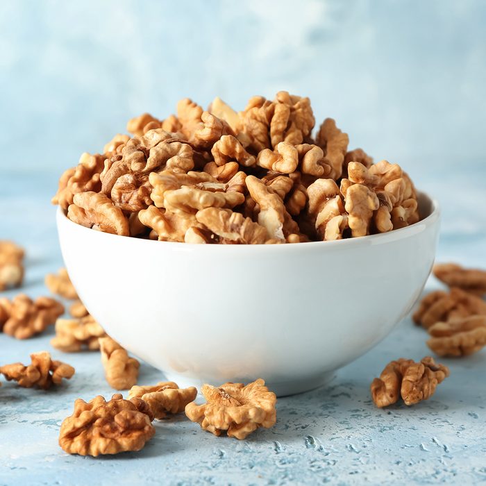 Bowl with tasty walnuts on color table