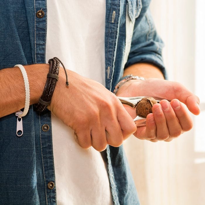 Hands of young man cracking nut with nutcracker at home. Healthy diet