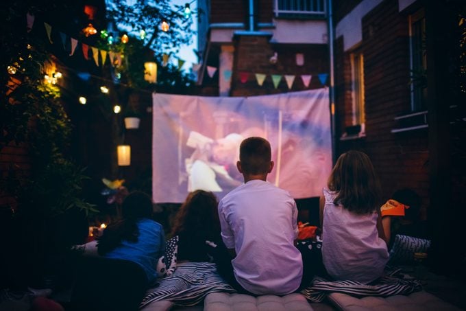 Group of children on movie night in backyard. Sitting, eating pizza and watching movie.