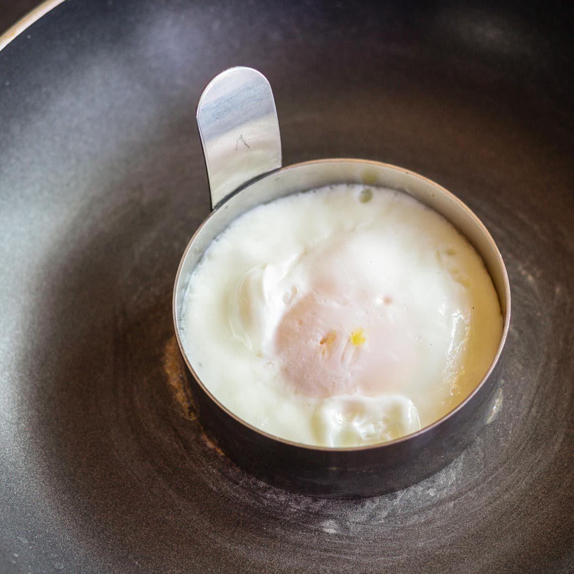 round egg cooking in a pan for Copycat Mcdonalds Egg Mcmuffin recipe