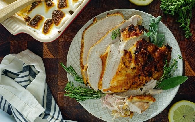 carved air fryer turkey breast on a platter with herbs and sweet potato casserole overhead