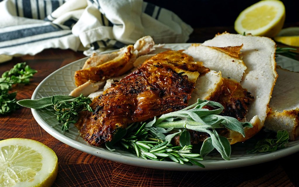 profile shot of air fryer turkey breast on a platter with herbs and lemon