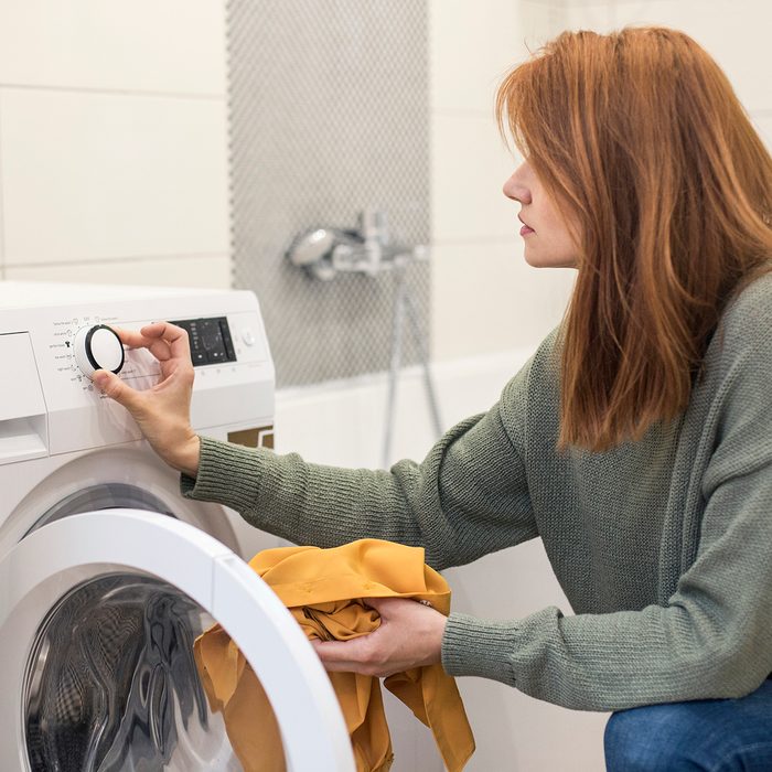 Young woman doing laundry, setting a washing machine. About 25 years old, Caucasian female.