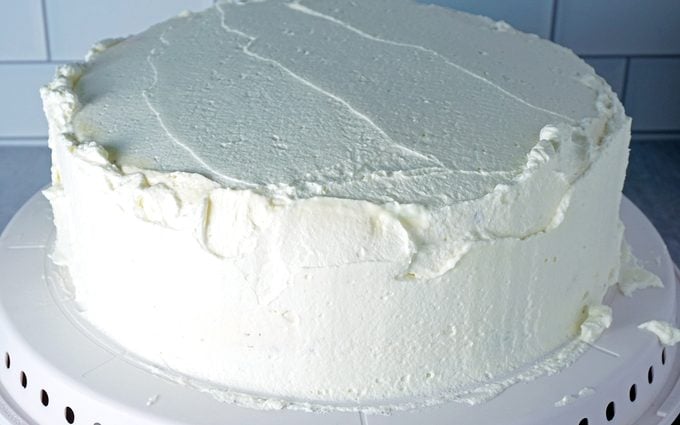 spreading a thin layer of whipped cream frosting onto ice cream cake
