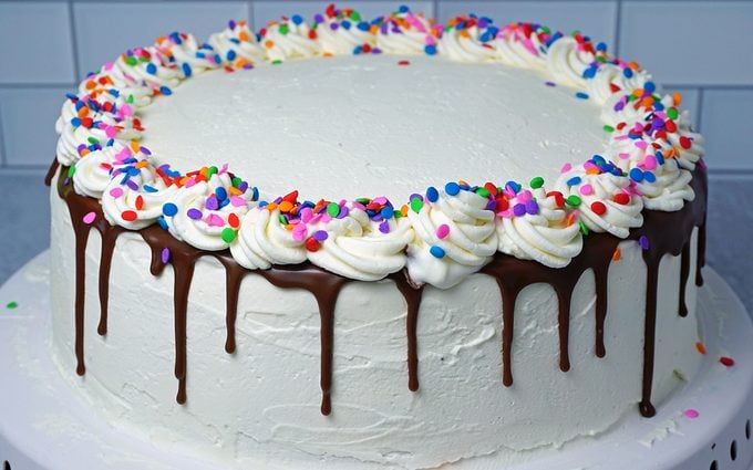 adding a ribbon of whipped cream icing to ice cream cake with rainbow sprinkles