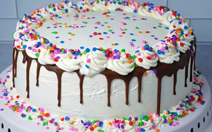 adding a ribbon of whipped cream icing to ice cream cake with rainbow sprinkles 2