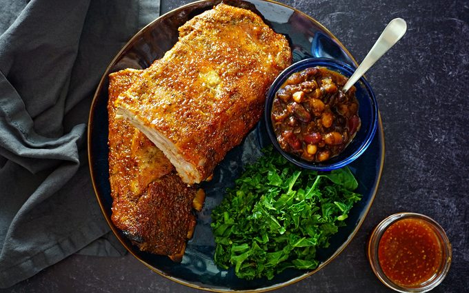 a platter of juicy oven ribs with a side of baked beans and greens overhead