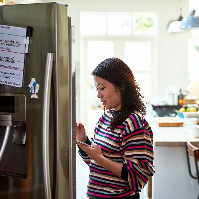 Mid adult woman checking food in fridge holding tablet