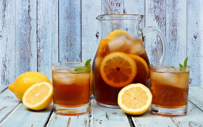 Pitcher of iced tea with two glasses and lemons on rustic blue wood background